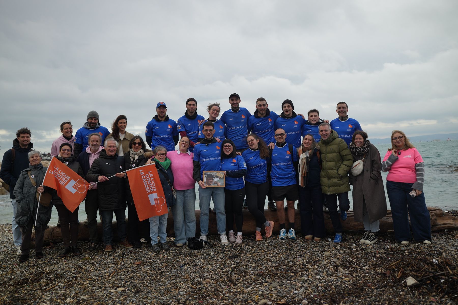 L'équipe Courir pour la Vie en maillots bleus, avec des bénévoles de la Ligue contre le cancer, sur une plage de galets